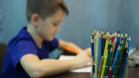 The boy draws with pencils sitting at the table. boy in out of focus, pencils in Stock Footage 145210347
