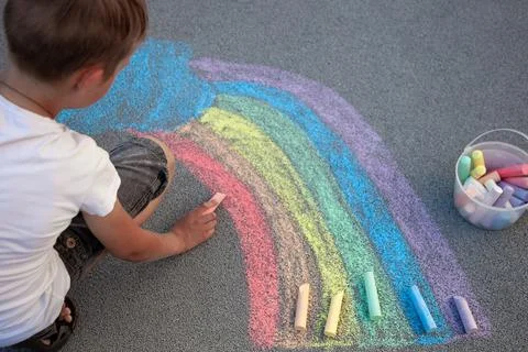 A boy draws a rainbow with multi-colored chalk on the asphalt. Drawing Stock-Fotos