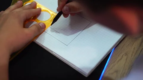 Boy draws simple drawing of house with pencil and ruler in squared notebook. han Stock Footage 307121726