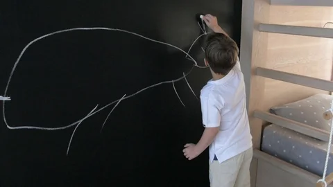 Boy draws on the slate wall in the nursery. child draws on black wall with chalk Stock-Footage 107893359