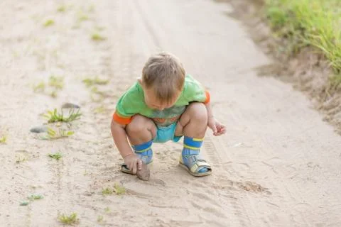 Boy draws with a stone on the sand while squatting on a sandy village road Foto stock