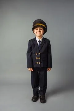 Boy dressed in a black pilot uniform stands at the gray background Stock Photos