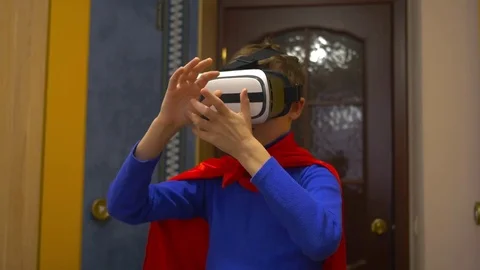 A boy dressed as a superhero in virtual reality glasses plays at home Vidéo 85100482