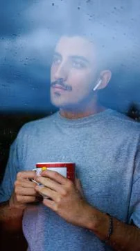 Boy drinking from a cup some drink while looking out the window wet with drop Stock Photos