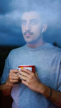 Boy drinking from a cup some drink while looking out the window wet with drop Stock Photos