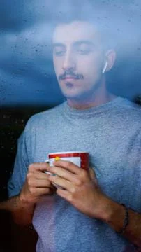 Boy drinking from a cup some drink while looking out the window wet with drop Фото