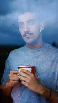 Boy drinking from a cup some drink while looking out the window wet with drop Stock Photos