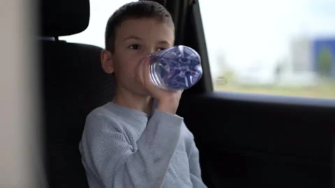 Boy drinking fresh water from a plastic bottle in the car. The child rides in a Stock Footage 208818557