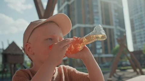 Boy Drinking from Plastic Bottle in Urban Park with Tall Buildings and Vídeos de archivo 345968966