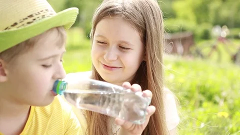The boy is drinking water from the bottle. Cheerful brother and sister.  Stock Footage 76497484