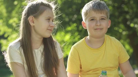The boy is drinking water from the bottle. Cheerful brother and sister.  Stock Footage 76780157
