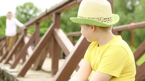 The boy is drinking water from the bottle. The children are sitting on the bridg Stock Footage 76497425