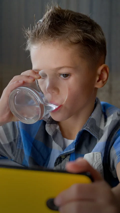 Boy Drinking Water from Glass While Concentrating on Smartphone Stock Footage 320635835