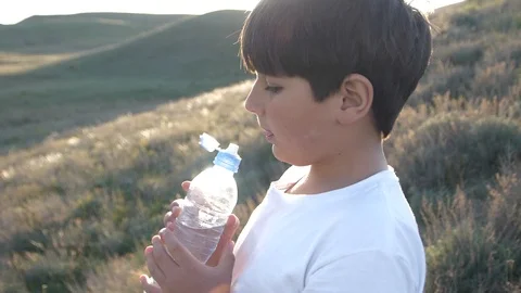 Boy is drinking water from plastic bottle on sunset Sun rays pass thru Stock Footage 90673444