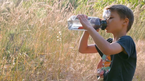 Boy drinks cold water from a plastic bottle on a walk. Stock Footage 311261272