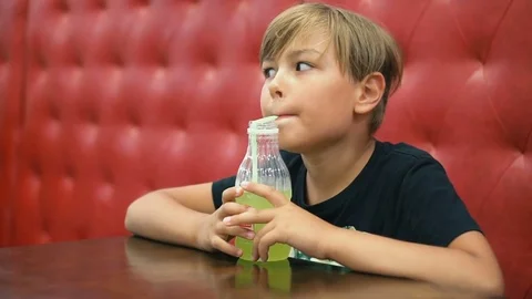 A boy drinks lemonade in a cafe on a red couch Stock Footage 79279153