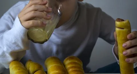 A boy drinks milk and eats sausage in a dough. Stock Photos