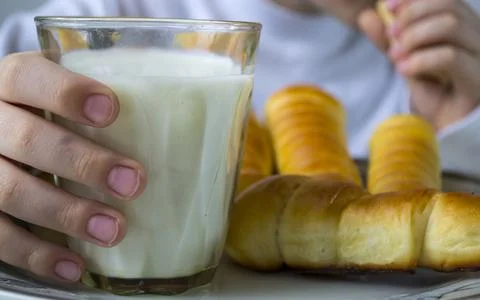 A boy drinks milk and eats sausage in a dough. Stock Photos