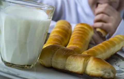 A boy drinks milk and eats sausage in a dough. Stock Photos
