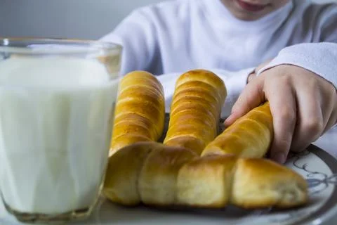 A boy drinks milk and eats sausage in a dough. Stock Photos