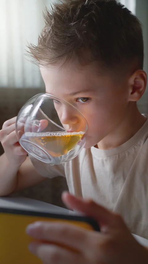 A boy drinks warm tea from a glass mug and uses a smartphone Stock Footage 320636069