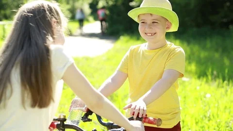 The boy drinks water from a bottle. Boy and girl on bicycles in the park.  Stock Footage 76779841