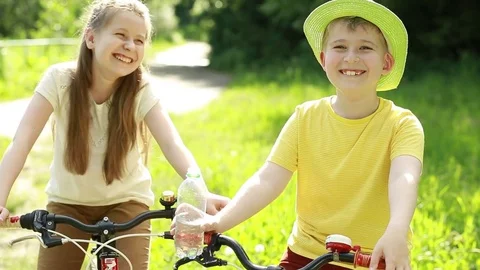 The boy drinks water from a bottle. Boy and girl on bicycles in the park.  Stock Footage 76779924