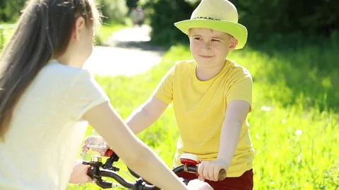 The boy drinks water from a bottle. Boy and girl on bicycles in the park.  Stock Footage 76779933