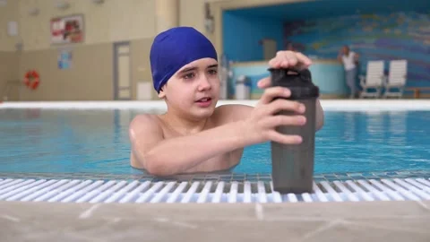 The boy drinks water from a bottle at the edge of the pool Stock Footage 145756535