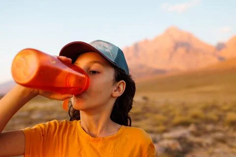 Boy drinks water from a bottle while traveling in the mountains. the child dr Stock Photos