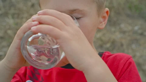 A boy drinks water from a glass, which is shown in close-up. Stock Footage 274960870