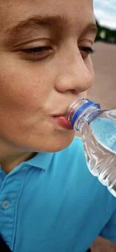 Boy drinks water from a plastic bottle in an outdoor setting Stock-Fotos