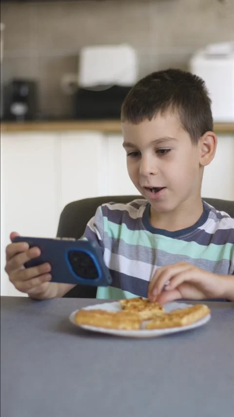 Boy eating cookie and looking at smartphone Stock Footage 342238773