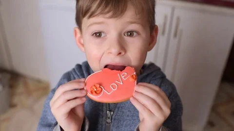Boy eating a gingerbread in the shape of a heart with the inscription "love" Stock Footage 85261697