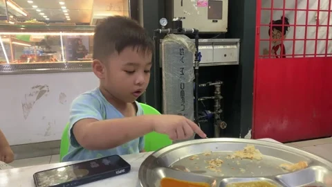 A boy eating roti canai while looking at his mobile phone Stock Footage 285836792