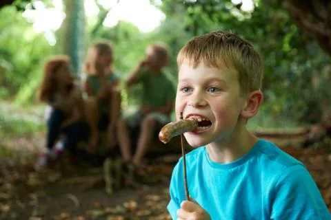 Boy Eating Sausage Cooked On Campfire With Friends Stock Photos