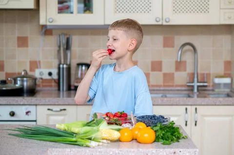 Boy eating strawberry at kitchen table with fresh produce Stock Photos