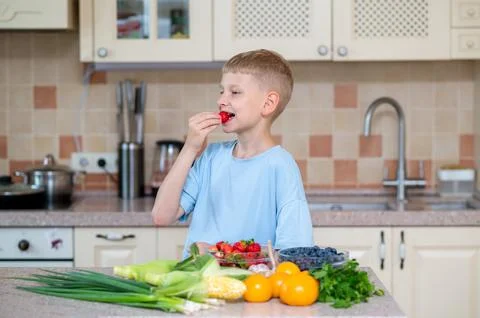 Boy eating strawberry at kitchen table with fresh produce Stock Photos