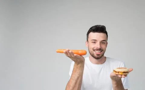 Boy eats an carrot and hamburger. Man makes the choice between fast and healthy Фото