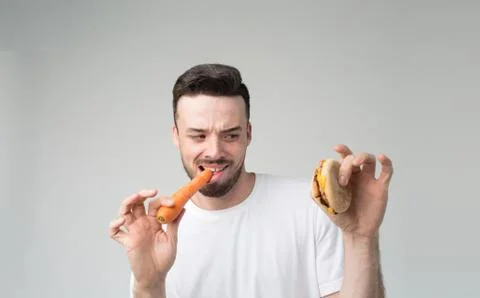 Boy eats an carrot and hamburger. Man makes the choice between fast and healthy Stockfoto's