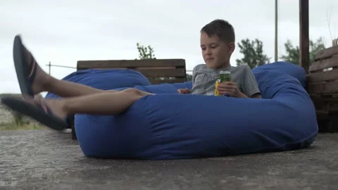 A boy eats cookies lying on a bag chair. a soft sofa on the street. the pleasure Stock Footage 167722360