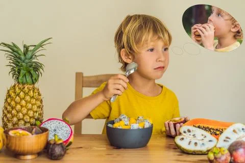 Boy eats fruit but dreams about hamburger. Harmful and healthy food for children Stock Photos