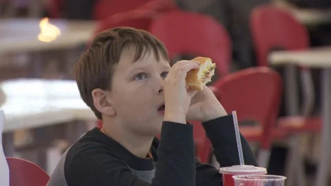 Boy eats a hamburger. close-up. food court in the mall.  watching TV Stock Footage 113800971