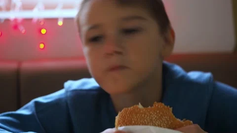 A boy eats a hamburger in a wrapper. in the foreground is a hamburger. the boy Stock Footage 167451908