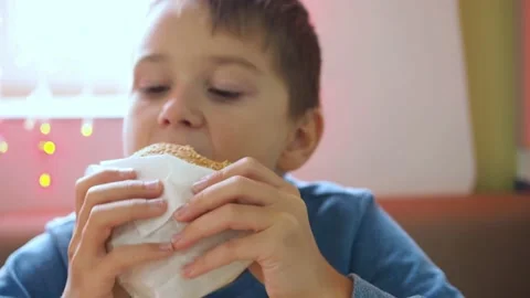 A boy eats a hamburger in a wrapper. in the foreground is a hamburger. he takes Stock Footage 167663280