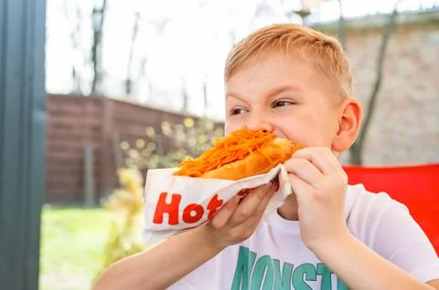 A boy eats a hotdog at a table in a cafe in a spring park Stock Photos