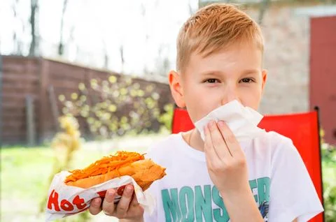 A boy eats a hotdog at a table in a cafe in a spring park Stock Photos