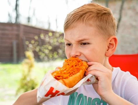A boy eats a hotdog at a table in a cafe in a spring park Stock Photos