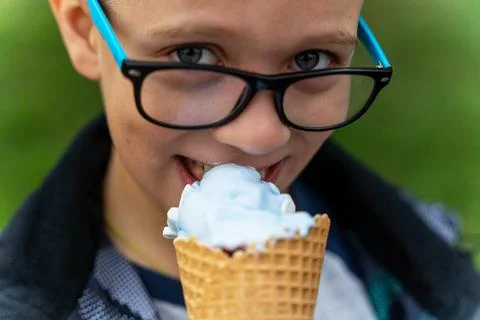 Boy eats ice cream in a waffle cone on the street in the park Stock Photos