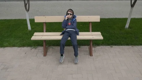 Boy eats Lollipop and shakes her legs on the bench near the house. Top view. Stock Footage 130117959
